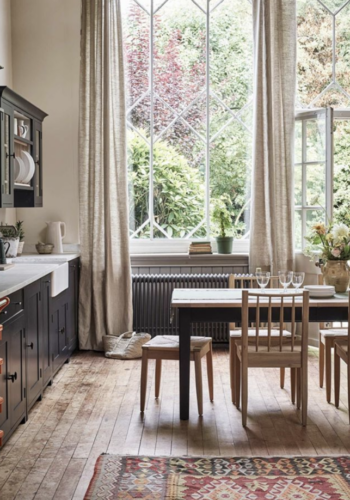 Black kitchen cabinets, large windows with natural linen curtains and wooden dining table and chairs by Neptune.