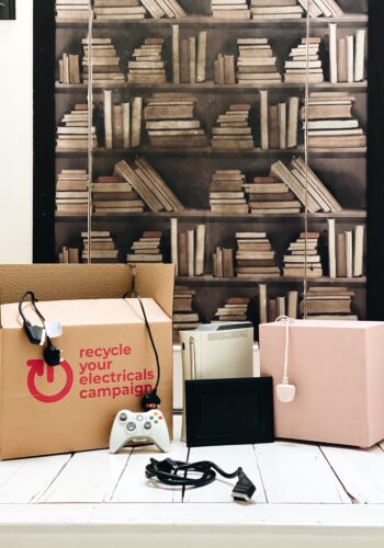 Boxes of electricals in front of book shelf for Giveback January – Recycle or Donate Unwanted Electrical Goods