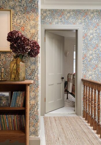 Hallway landing with dark wood banister, jute floor runner, William Morris wallpaper in soft tones, wooden bookcase.image by @home_stead