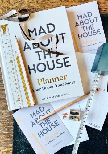 Mad About the House, new book scattered with stationery and tape measure on wooden table.