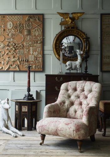 pale green panelled wall, antique mirror and statue, faded floral button back armchair by Drew Pritchard for Barker and Stonehouse